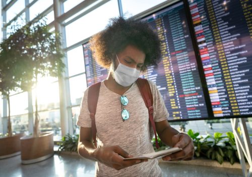 male traveler wearing a facemask at the airport with the flight schedule