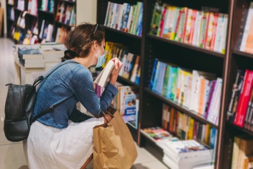 Woman with protective face mask choosing a book in the bookstore