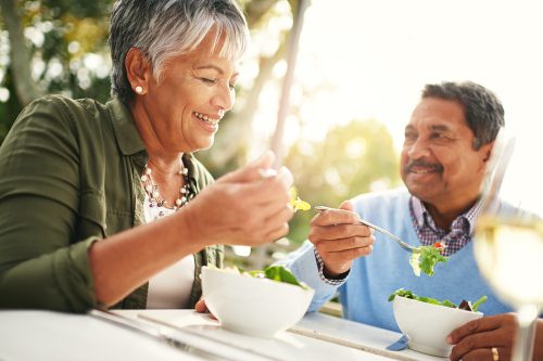 A middle-aged couple eating greens at a table outdoors