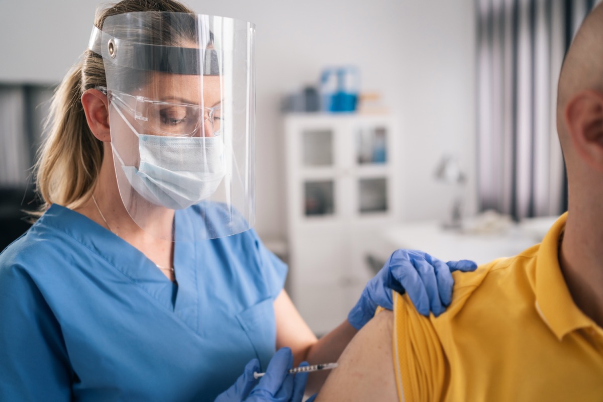 Female doctor wearing face shield and gives a COVID-19 vaccine to a patient