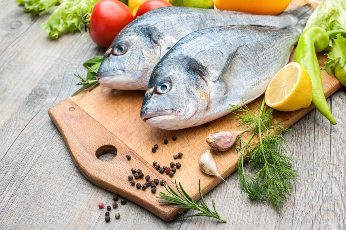 two raw whole fish on wooden cutting board