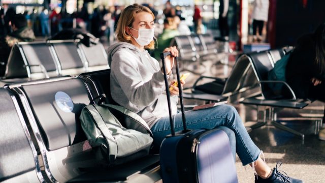 A female passenger in a medical mask is waiting for a flight at the airport.