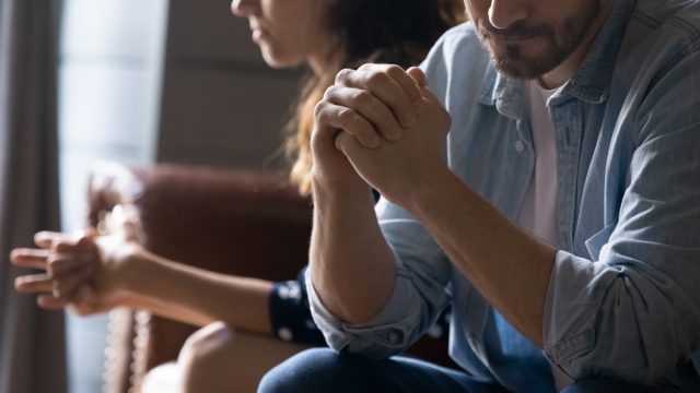 young couple sitting on couch looking unhappy due to argument over infidelity or cheating