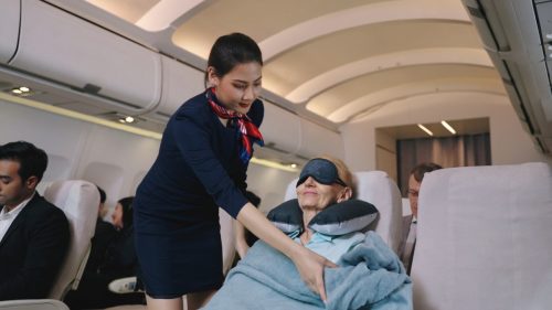 Flight attendant helping woman on plane with blanket
