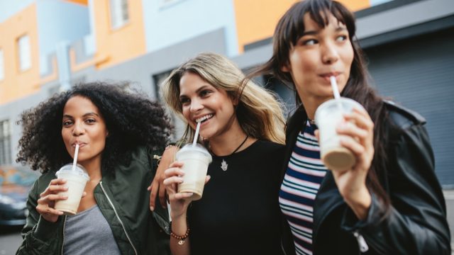Outdoors shot of three young females having ice coffee on city street.