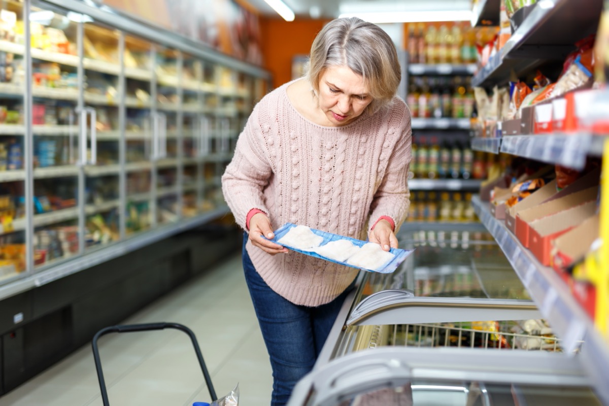 older woman looking at package of fish in supermarket