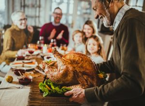 Happy senior man bringing Thanksgiving turkey to the table for his family's lunch.