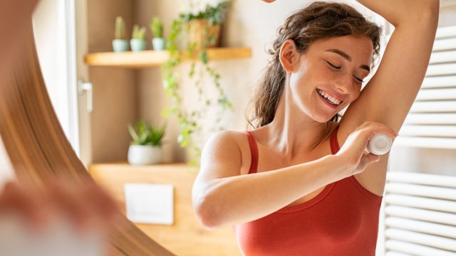 A young woman applying a stick of deodorant or antiperspirant to her underarm