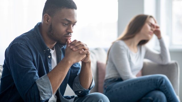 young man and woman in a couple looking upset at one another while sitting on couch