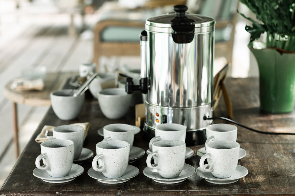 A communal coffee thermos in a hotel lobby with mugs
