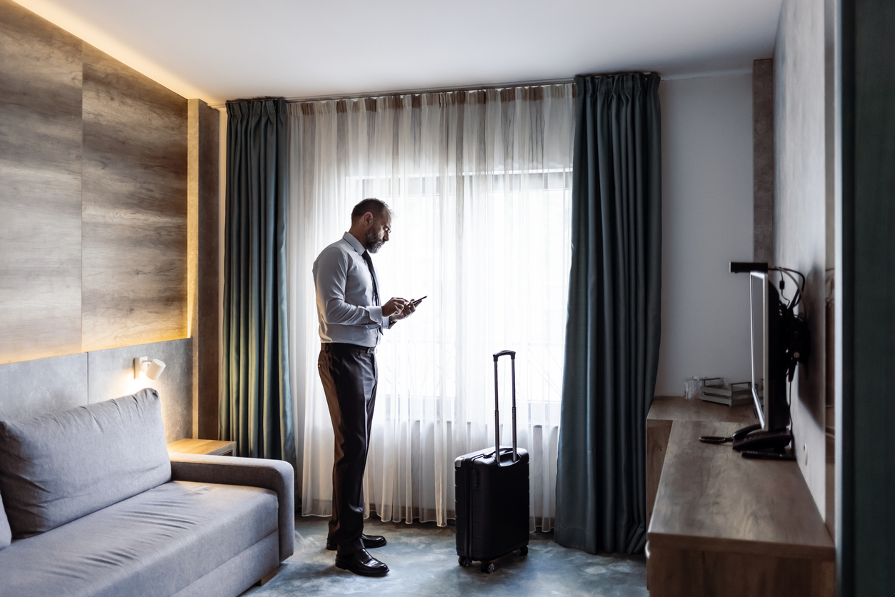 A man who appears to be a business traveler standing in a hotel room using his phone