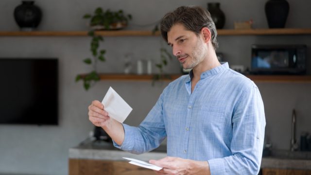 Man at home checking letters in the mail and smiling – domestic life concepts