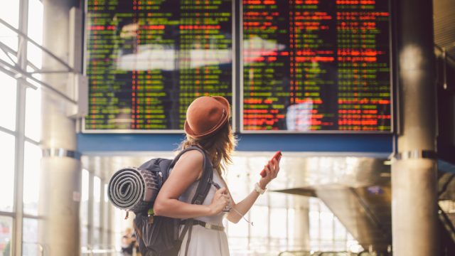 A woman at the airport checking when her flight leaves while carrying her luggage