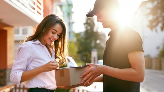 A young woman signing for a package being delivered to her by a courier