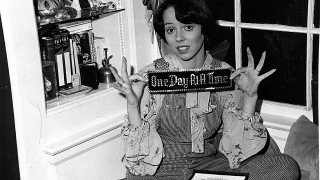mackenzie phillips holding a placard that says one day at a time