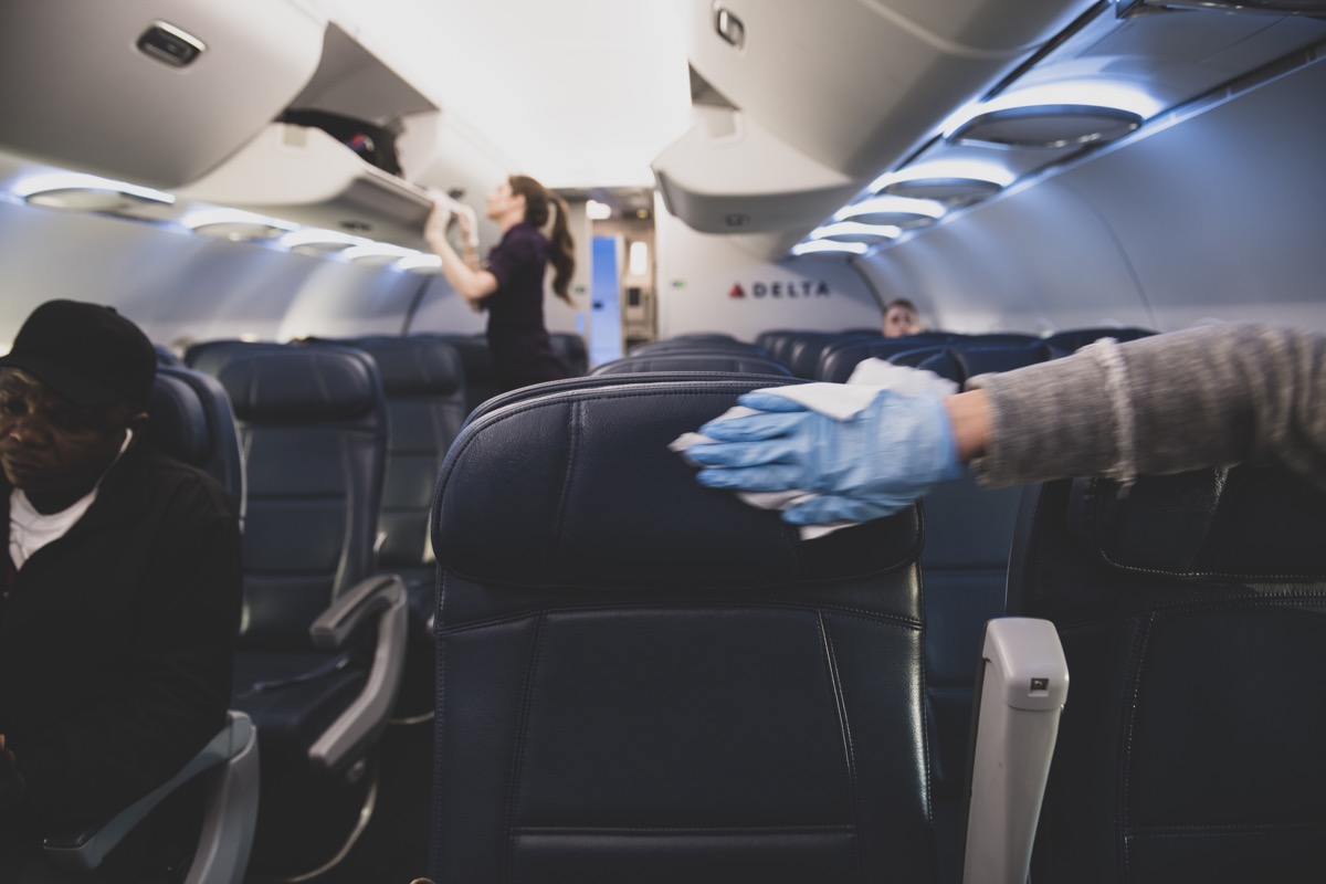 On a Delta flight from New York’s Laguardia Airport to Atlanta, a passenger who has just boarded wears a plastic glove while using a wipe to disinfect the airplane seats and armrests on her row. (March 21, 2020)