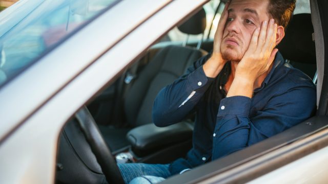 A young man driving a car and stuck in a traffic jam with a sad look on his face