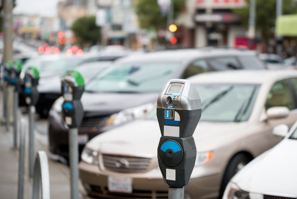 A row of parking meters in front of parked cars