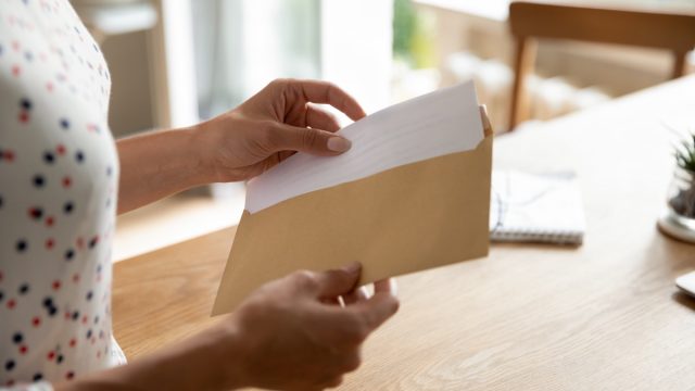 Postal correspondence. Close up view of young woman open paper letter message document prepare to read news view information. Female hands put written note in envelop before send it by mail to friend