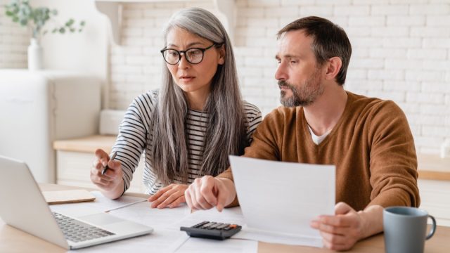 Mature middle aged couple family wife and husband counting funds, savings declarations, investments,paperwork, financial documents, bankruptcy, court case, bills, pension with laptop.