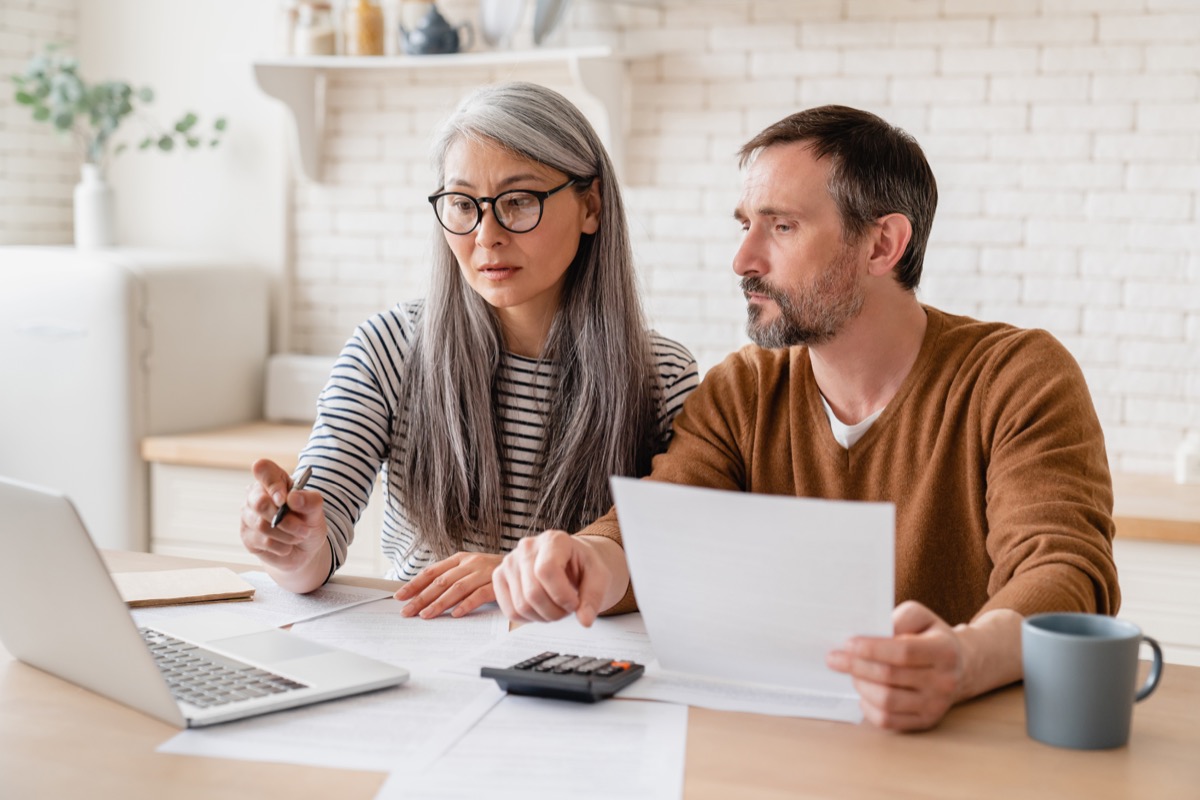 Middle-aged couple sitting at kitchen counter paying bills