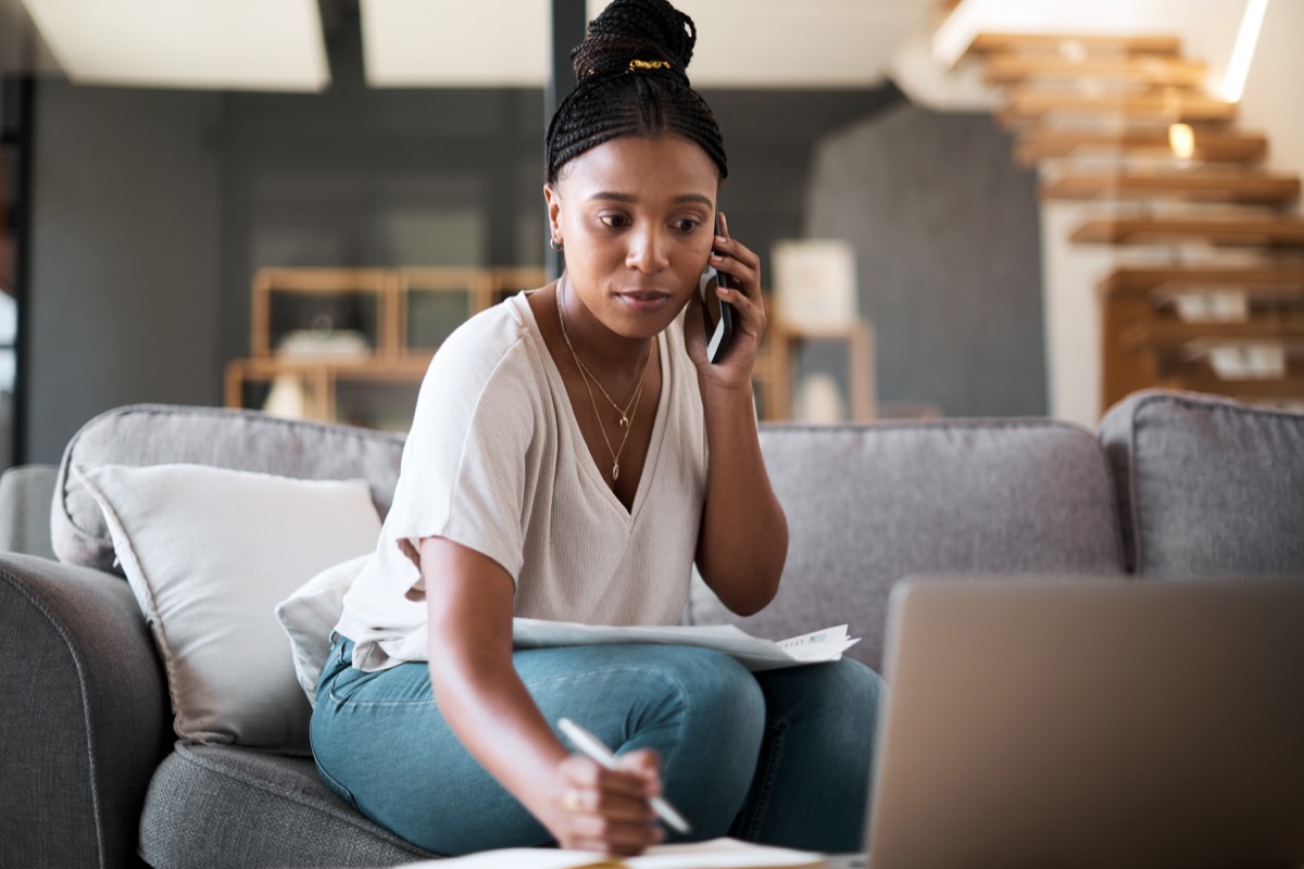 Shot of a young woman talking on a cellphone while going through paperwork at home