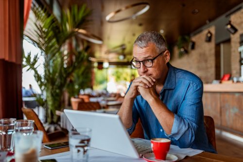 Contemplating businessman in the restaurant feeling sad. Full concentration on work. Confident mature man working on laptop while sitting at his working place in office.