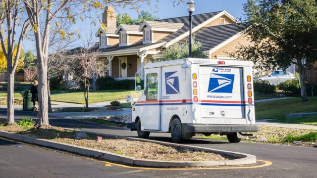 USPS vehicle driving through a residential neighborhood on a sunny day