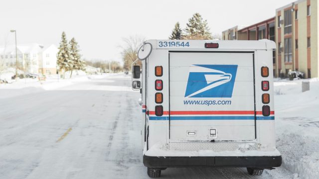 USPS, United States Postal Service, van parked on suburban street during winter with lots of snow.