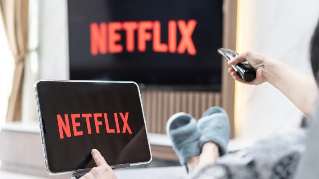 A person sitting on a couch watching Netflix on their TV and tablet