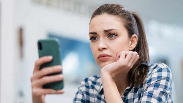 A young woman looking at a message on her phone with a concerned look on her face.