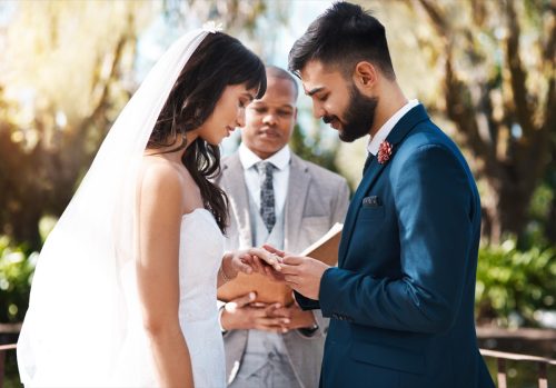 Cropped shot of an affectionate young groom slipping a ring on to his bride's finger while standing at the altar on their wedding day