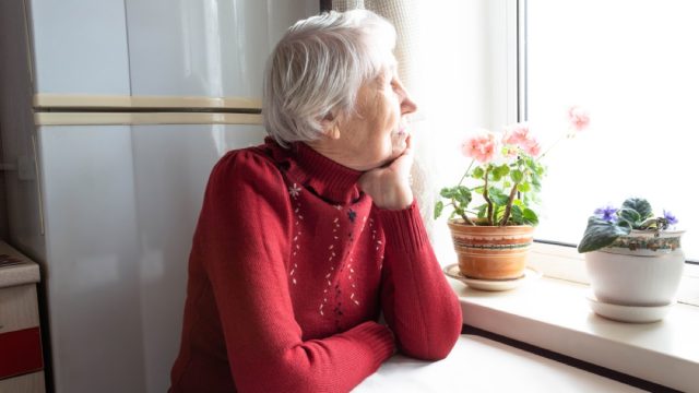 lonely older woman staring out the window next to flowers