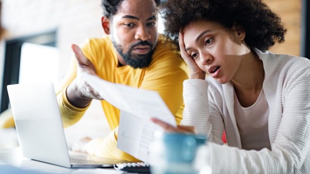 couple feeling frustrated while paying their bills over laptop at home