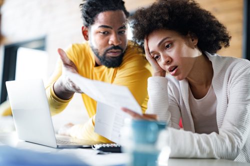 couple feeling frustrated while paying their bills over laptop at home