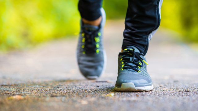 Closeup of a man's sneakers while he walks outside on a paved path