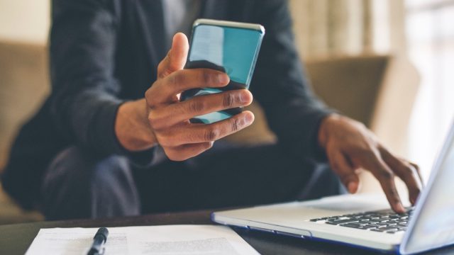 Cropped shot of an unrecognizable man using a smartphone and a laptop while working from home