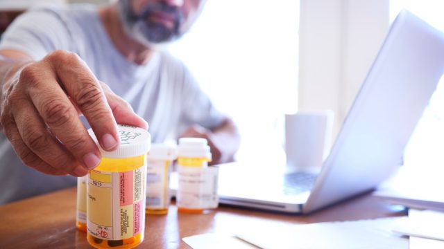man in his late fifties reaches for one of his prescription medication bottles as he sits at his dining room table