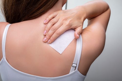 Rear View Of Woman Sticking Patch To Help With Stiff Neck