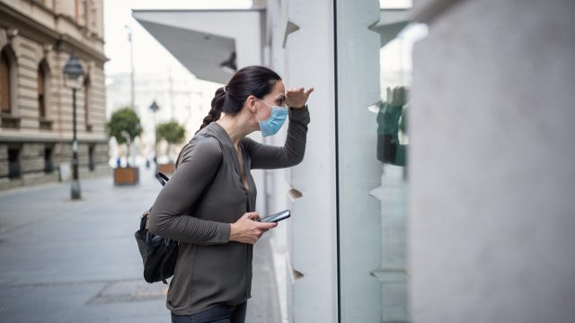Woman wearing protective mask, using mobile phone. She is outdoors, in a street. Belgrade, Serbia