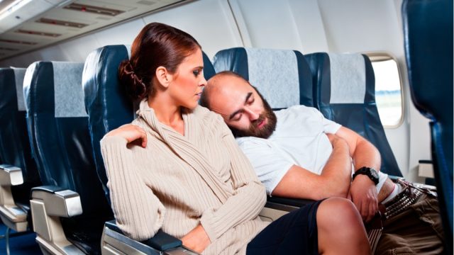 man sleeping on woman's shoulder on airplane