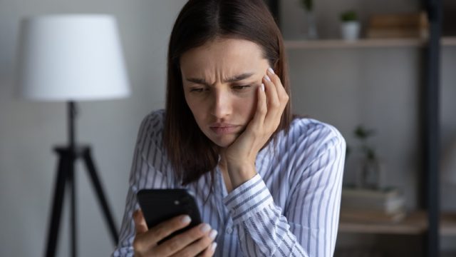 woman looking annoyed and upset with her hand on her face and her phone in her hand
