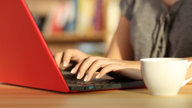 Close up of girl hands writing in a red laptop on a table at home with a warm light and a colorful background