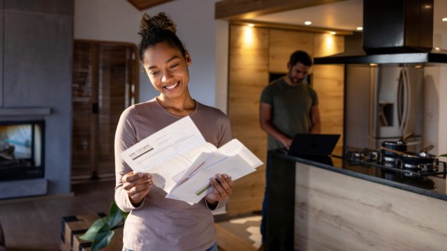 woman at home looking at a utility bill that came in the mail and smiling
