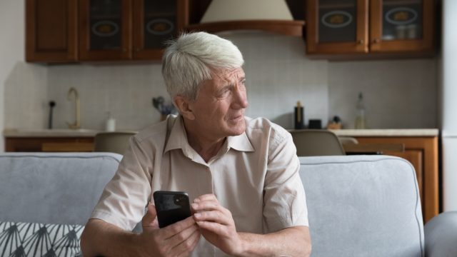 A senior man holding a smartphone with a concerned look on his face