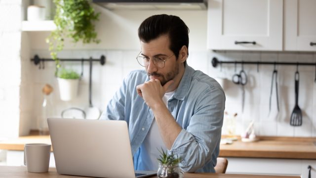 A young man sitting in his kitchen using a laptop to check his email