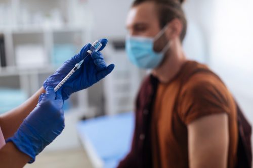 Young man waiting to get his vaccine by an unrecognizable nurse in the hospital