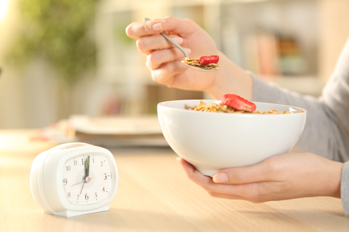 woman waiting to eat bowl of cereal with clock for intermittent fasting