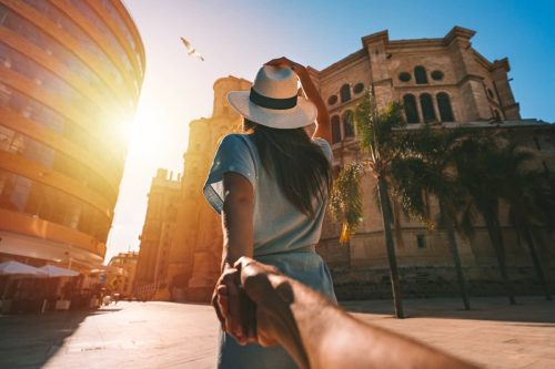Woman in a hat leading a man through a European city
