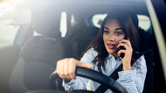 Woman In Car Talking On Mobile Phone Whilst Driving. Attractive woman uses smart phone while driving.